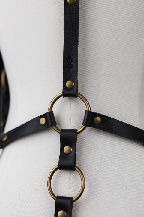 Black leather harness with gold rings on a mannequin against a white background