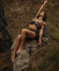 Woman in a natural setting, sitting on a rock wearing bijou by juju's black leather corset