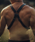 Back view of man wearing Bijou by Juju black leather suspenders with brass hardware in a natural outdoor setting.